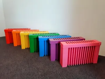 Sieben Flächenspeicherheizungen in Regenbogenfarben nebeneinander