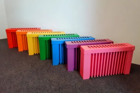 Sieben Heizungen in Regenbogenfarben nebeneinander